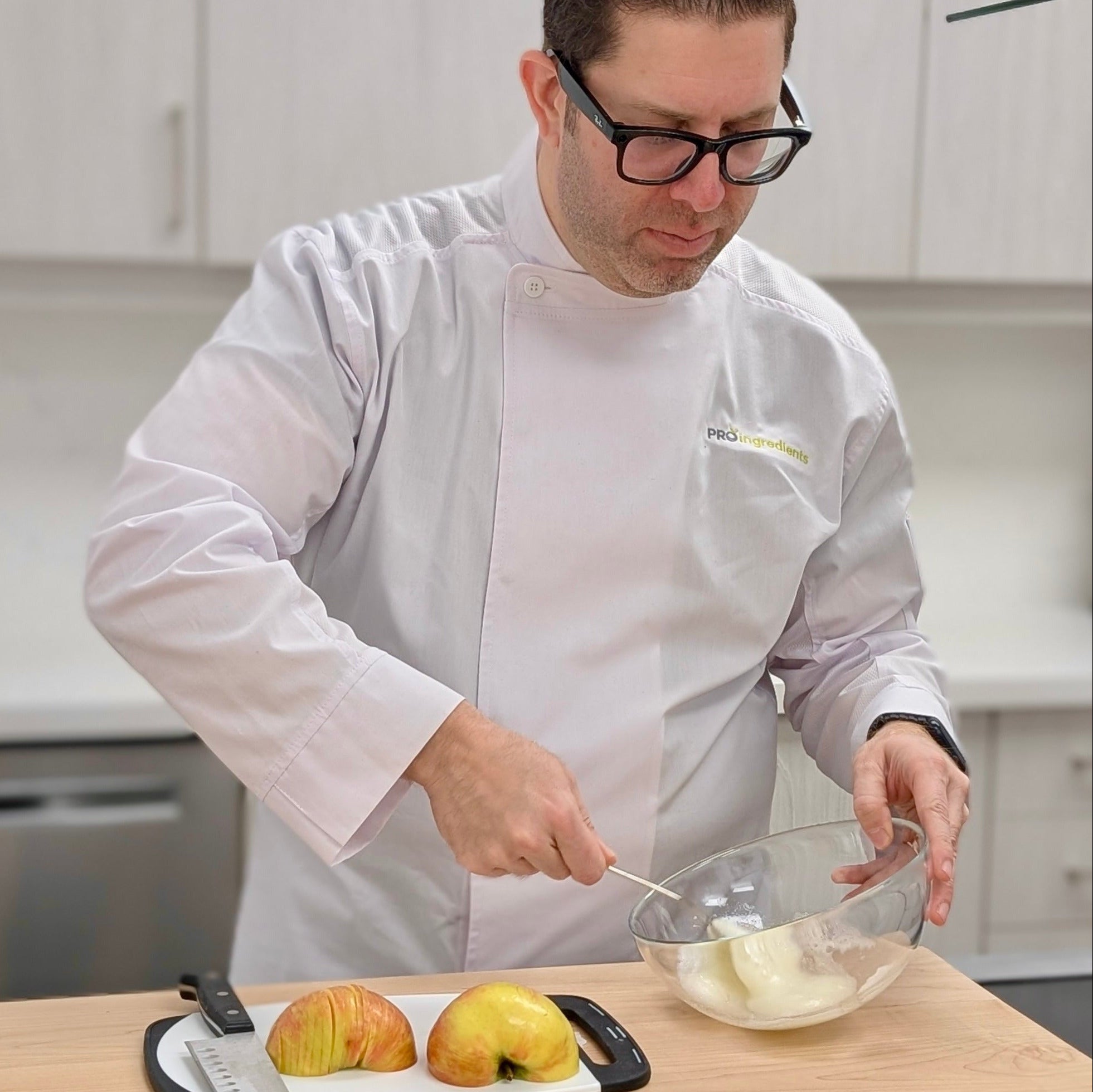 Chef preparing food in a kitchen with apples and a bowl on a counter.