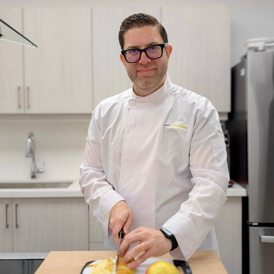 Man in a kitchen wearing a white chef's coat, cutting vegetables on a cutting board.